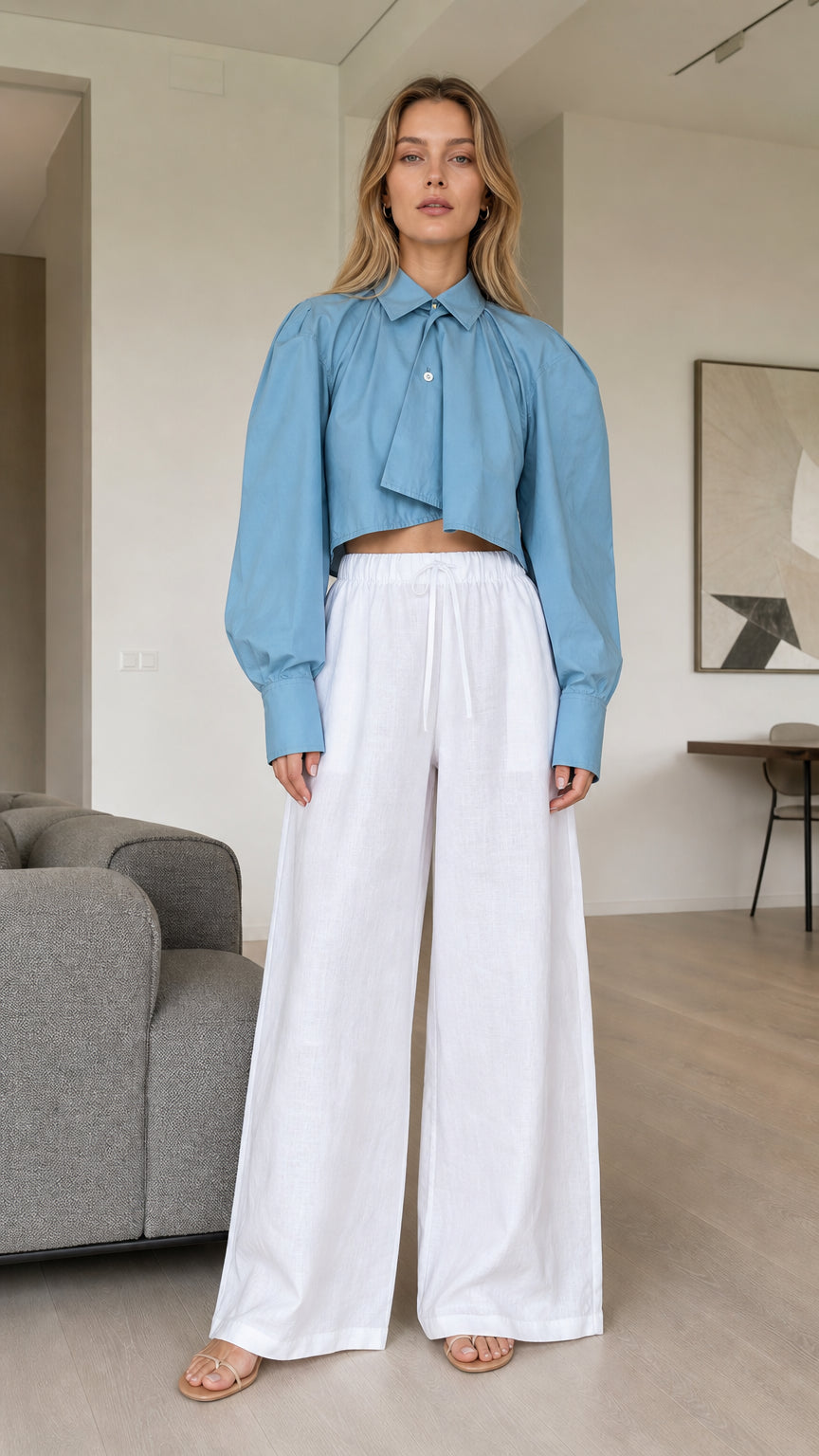 Front view of model wearing dusty blue cropped pleated long sleeve shirt with white trousers