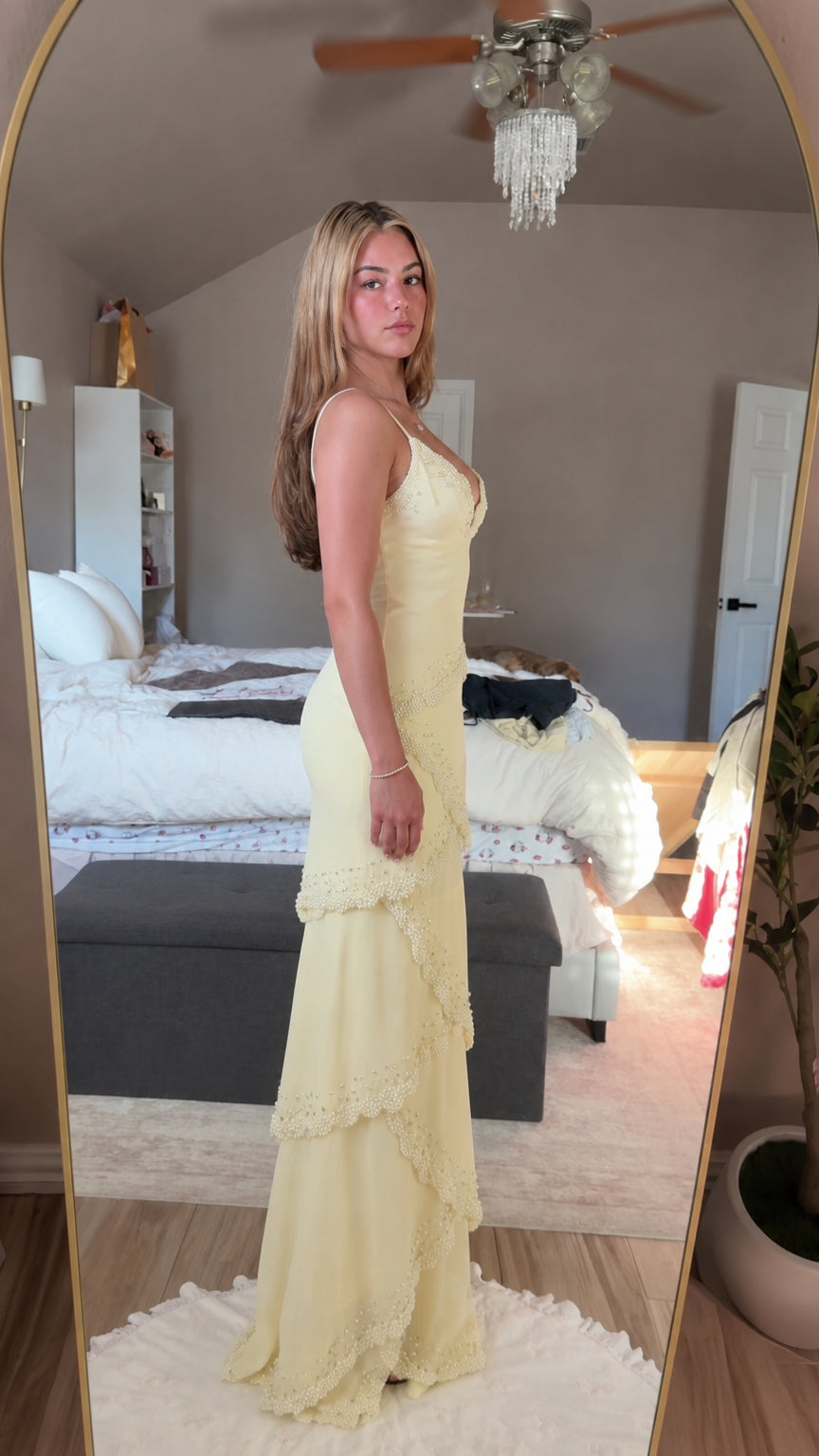 Side profile view of model wearing pastel yellow tiered evening gown
