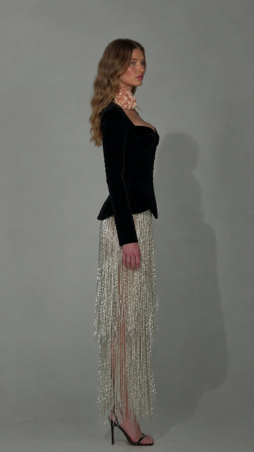 Side profile of black velvet corset evening dress with flowing tassel skirt