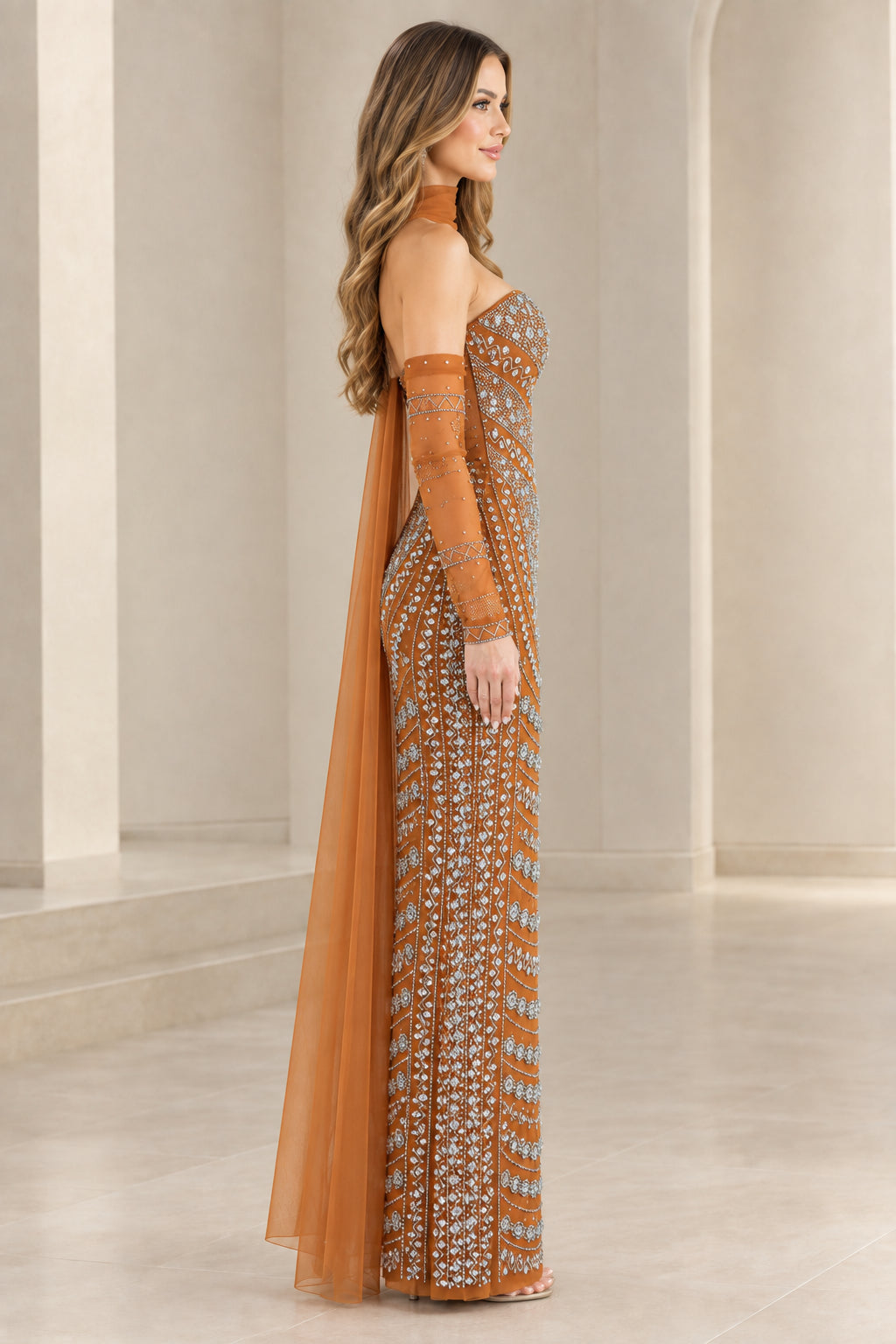 Side profile of rust orange embellished column formal gown with flowing tulle cape