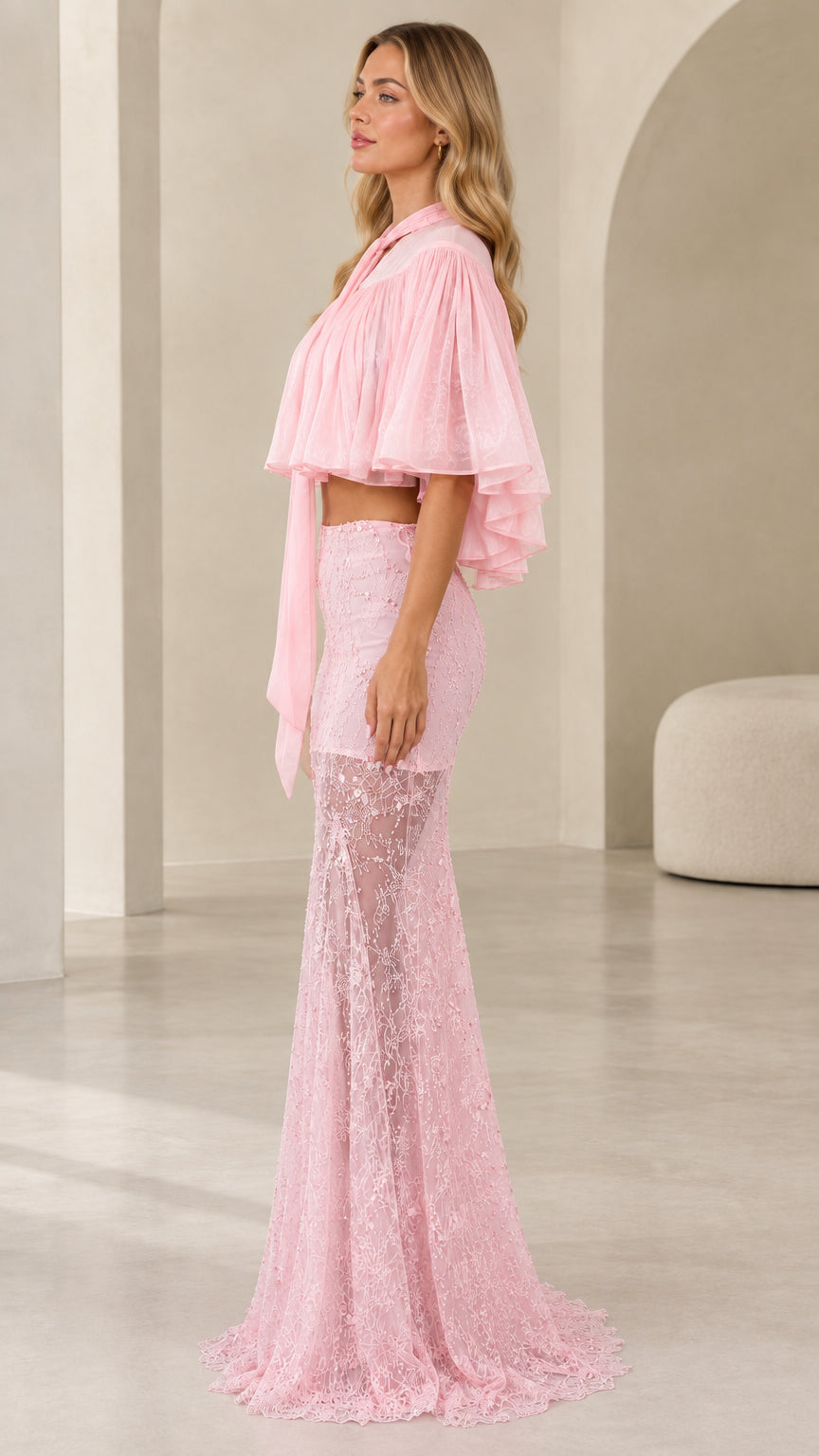 Side view of model in pink sequined lace mermaid skirt and flowing capelet set