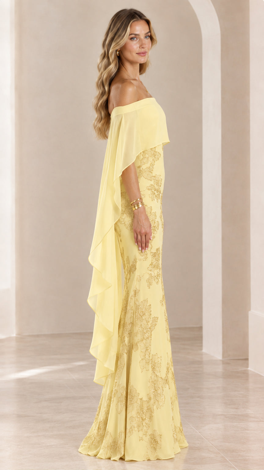 Side profile of woman wearing yellow floor-length formal dress with sheer cape overlay