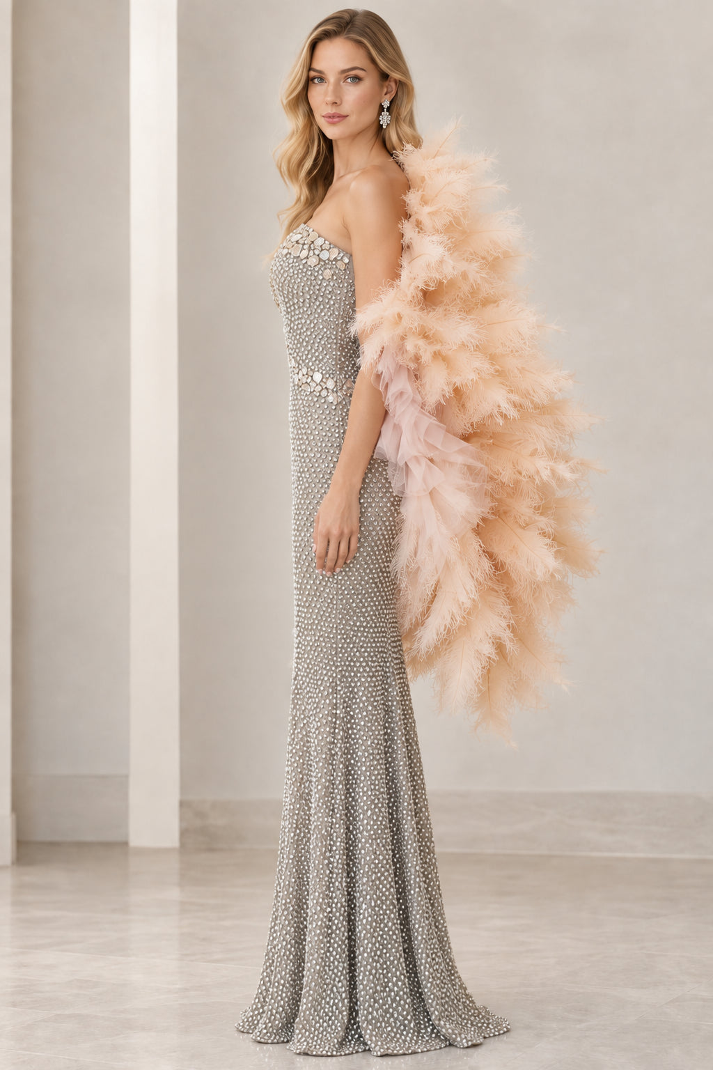 Side profile of model in full-length silver beaded formal dress and dramatic feather cape