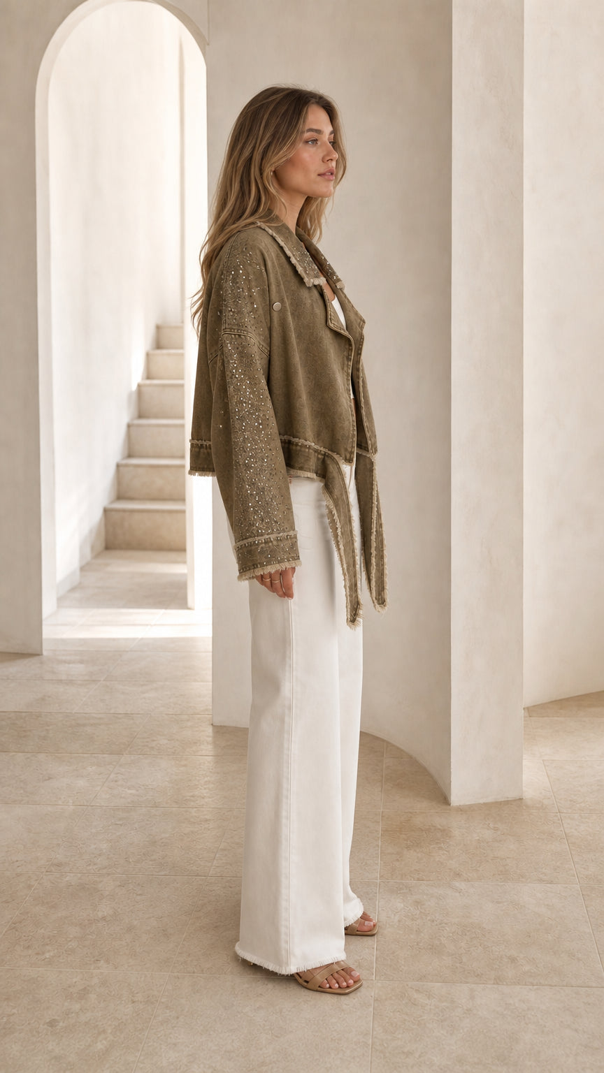 Side profile of model wearing olive green rhinestone fringe jacket with white trousers