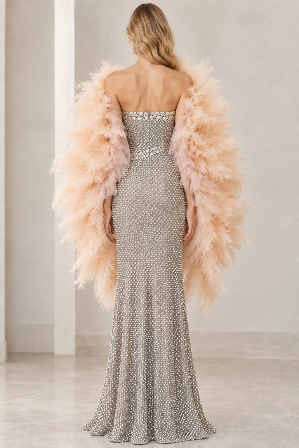 Back view of model showcasing the sleek back fit of the silver strapless evening gown with feather shawl