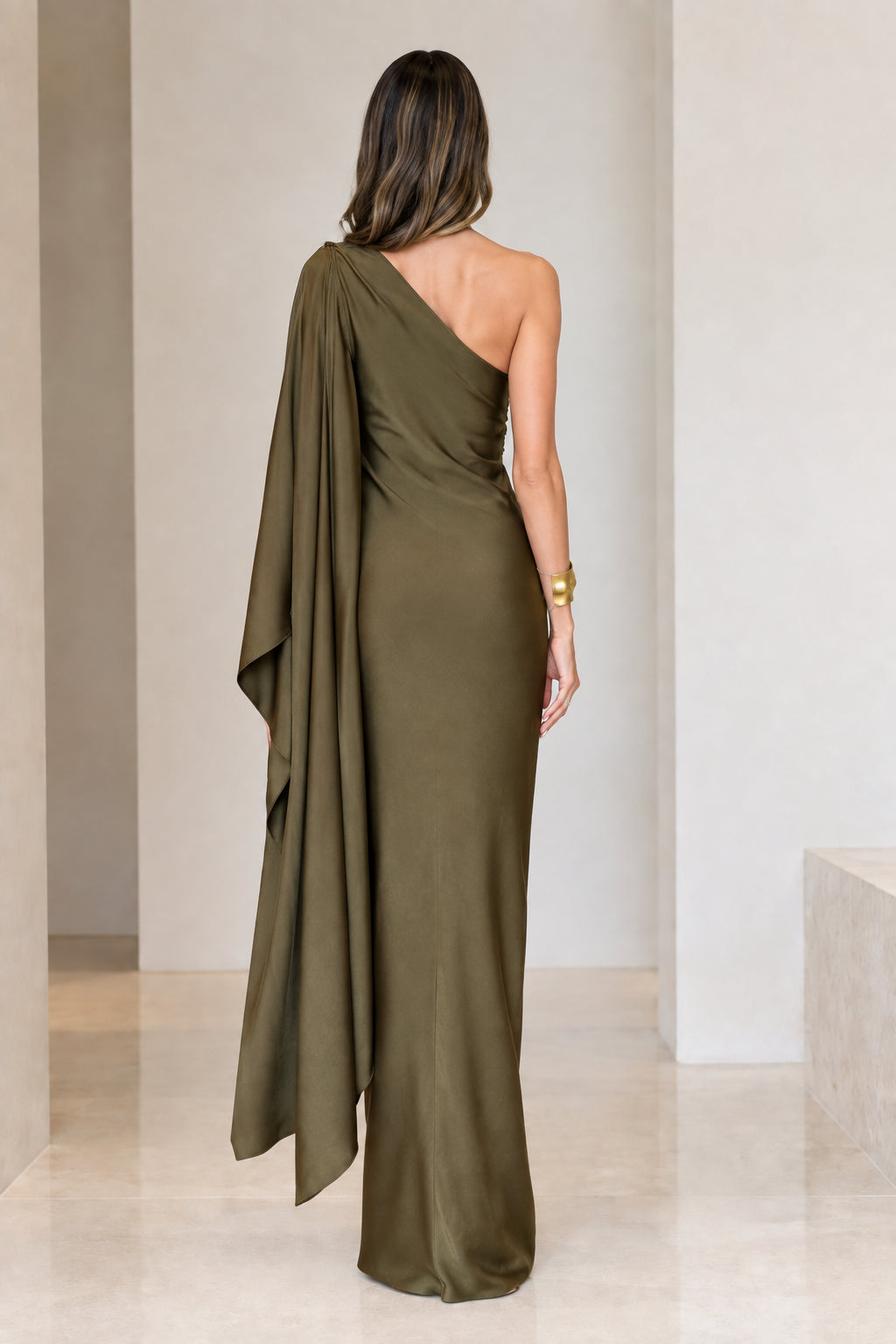 Back view of model in olive green one-shoulder satin gown showing draped back and cape sleeve