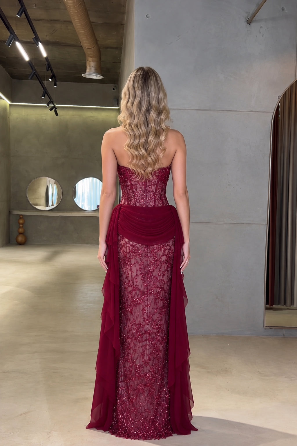 Back view of model wearing burgundy strapless corset gown with draped back train