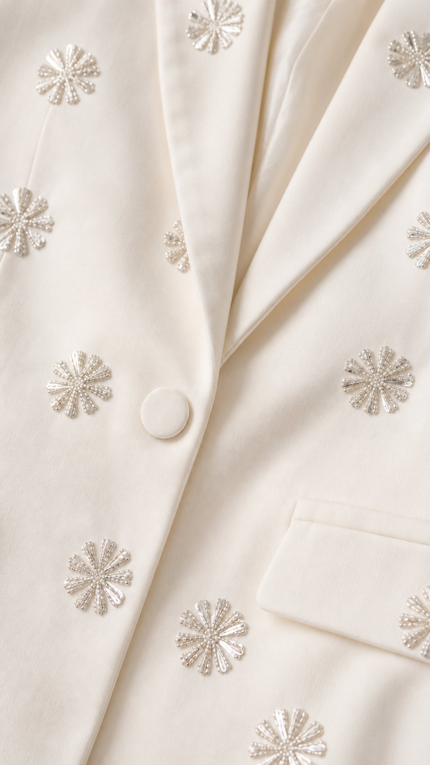 Close-up detail of rhinestone floral embellishments on cream blazer