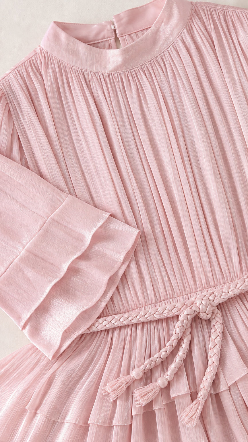 Close-up detail of blush pink pleated fabric, tiered cuff, and braided tassel belt