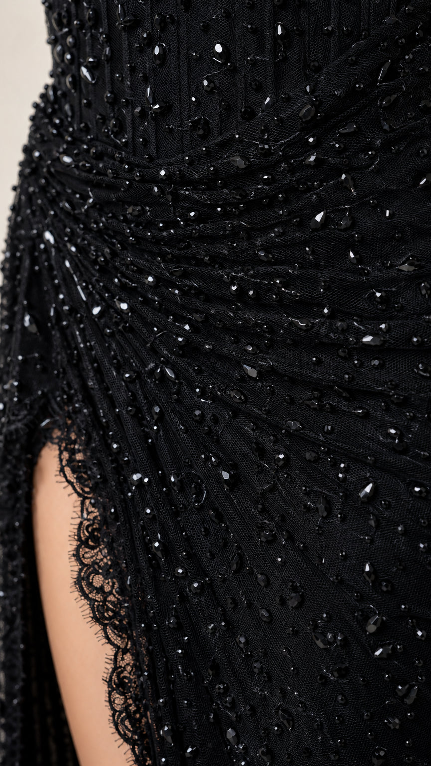 Close-up detail of black beaded gown fabric, ruched drape, and eyelash lace slit trim