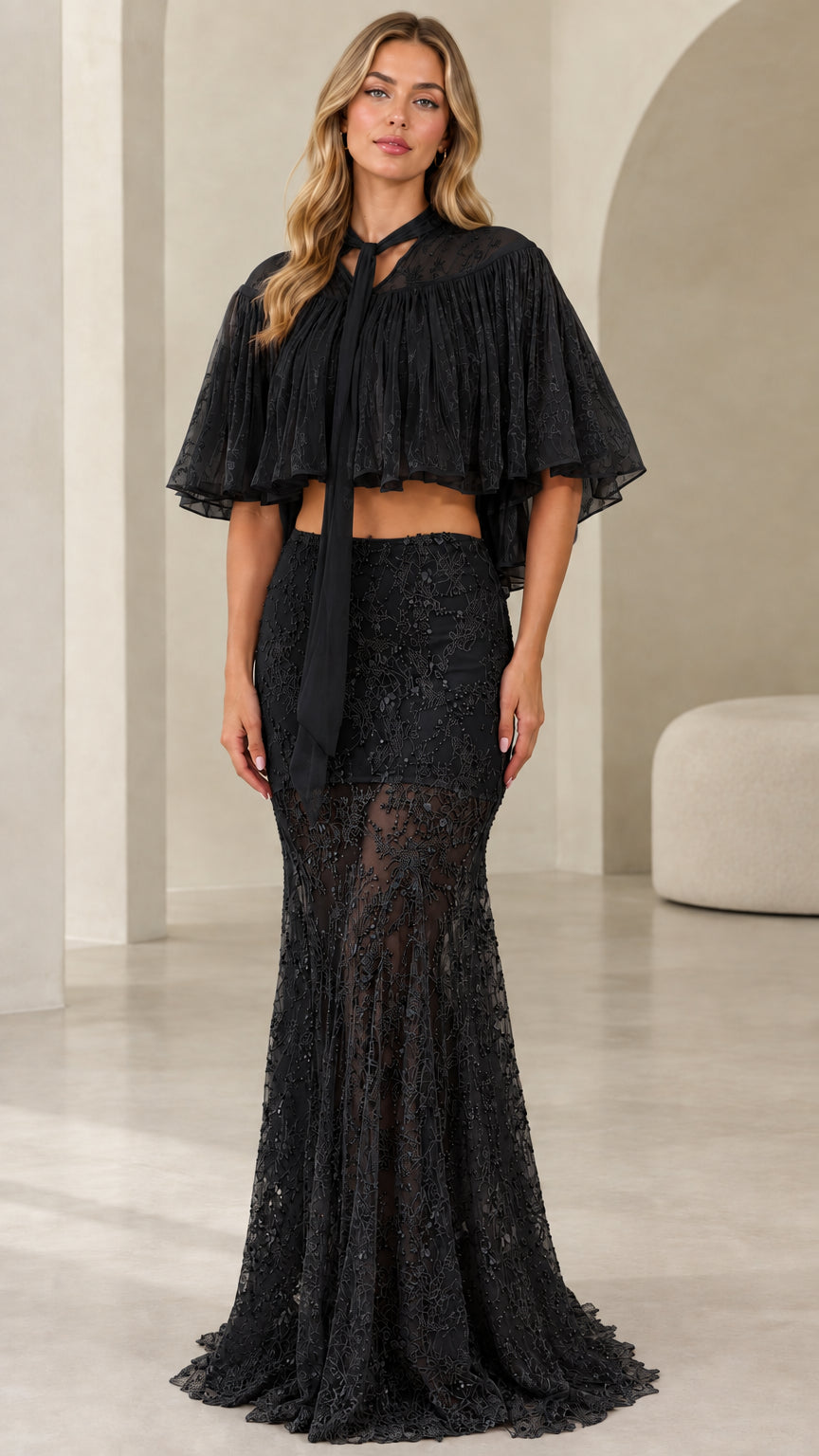 Model wearing black sequin lace two-piece evening gown with pleated capelet top
